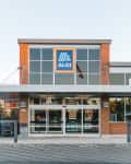 Front entrance of an Aldi store with sliding glass doors and a brick facade.