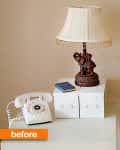 Vintage rotary phone, ornate lamp, and two white boxes on a table.