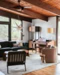 Living room with a black sofa, armchair, piano, and large windows overlooking a wooded area.