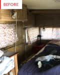 Messy camper bedroom with floral curtains, unmade bed, and wood paneling.