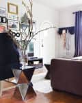 Living room with a geometric side table, vase with branches, gallery wall, and dark curtains.