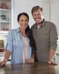 A couple smiling in a modern kitchen with white cabinets, farmhouse sink, and wooden countertop.