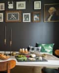 Dining room with dark walls, gallery wall art, white table, wooden chairs, and a spread of food and drinks.