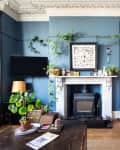 Eclectic living room with blue walls, floral armchair, fireplace, plants, and framed art.