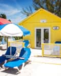 Yellow beach cabana with number 13, blue lounge chairs, and umbrella on sandy beach.