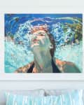Framed painting of a person underwater on a wall above a sofa with a striped pillow and a vase of flowers.