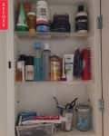 Cluttered bathroom cabinet with various toiletries, bottles, and toothpaste.
