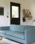 Living room with a blue sofa, black door, wall hooks with bags, and a staircase with plants.