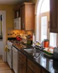 Yellow kitchen with wooden cabinets, black countertops, white appliances, and a red kettle on the stove.