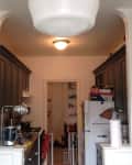 Narrow kitchen with dark cabinets, white fridge, and overhead light.