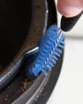 Cleaning a slow cooker rim with a blue brush to remove debris.