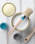 Paint cans in blue, green, and black with a brush and roller on a wooden surface.