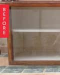 Empty wooden display cabinet with glass doors on a tiled floor.