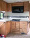 RV kitchen with wooden cabinets, stove, microwave, and sink. Fire extinguisher near the door.