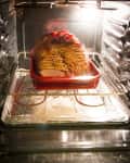 Sliced ham in a red baking dish inside an oven, illuminated by the oven light.