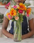 Person arranging a colorful bouquet of flowers in a glass vase on a kitchen counter.