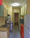 Narrow kitchen with green and yellow cabinets, tiled floor, and a small stove.