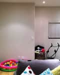 Living room with exercise bike, basket of clothes, ball pit, and colorful pillows on a gray sofa.