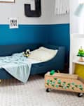 Children's room with a blue daybed, colorful toys, wicker chair, and a "High Five" wall sign.