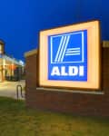 Aldi supermarket exterior at dusk with illuminated sign and parking lot.