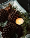 Pinecones and greenery arranged on a decorative plate with a lit candle.