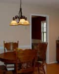 Dining room with wooden table and chairs, chandelier, and view into kitchen with stove and cabinets.