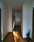 Long hallway with wooden floors, white walls, and multiple doors. An umbrella stand is visible on the right.