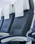 Three airplane seats with blue upholstery and white headrest covers, next to a window showing clouds.