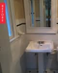 Small bathroom with pedestal sink, toilet, and glass shower door, featuring white tiles and a wall mirror.