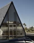 A-frame house with large glass front, slate roof, and surrounding plants on a sunny day.