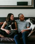 Couple sitting on a brown leather sofa with two dogs, next to a side table with a lamp.