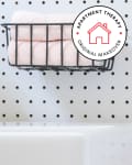 Black faucet and wire basket with folded towels on a pegboard wall.