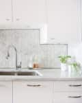Modern kitchen with herringbone tile backsplash, stainless steel sink, and potted plants on marble countertop.