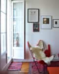 Open French doors in a room with framed art, red butterfly chair, and colorful rugs.