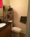 Small bathroom with wooden vanity, granite countertop, metal shelf with green towels, and a toilet.