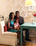Family sitting on a cream sofa with a turquoise table, floral wallpaper, and a lamp.