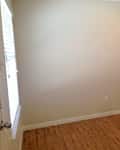 Empty room with beige walls, wooden floor, ceiling fan, and window blinds.