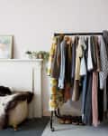 Clothing rack with assorted garments, blue armchair with cushions, and a dog resting on a fur-covered ottoman.
