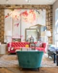 Eclectic living room with a pink tufted sofa, floral artwork, green chair, and decorative birdcage on a patterned rug.