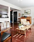 Living room with wooden floors, beige armchair, piano, coffee table, and wall art.