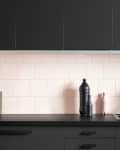 Modern kitchen with black cabinets, pink tile backsplash, black faucet, and decorative vases on the counter.