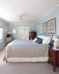 Bedroom with blue walls, a large bed with gray bedding, wooden nightstands, and framed floral art above the headboard.