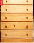 Plain wooden dresser with five drawers, round knobs, and small stickers.