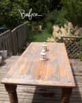 Weathered wooden table with three white lanterns on a deck, surrounded by greenery and a lattice fence.