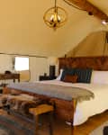 Glamping tent interior with a wooden bed, striped pillows, fur throw, desk, chair, and rustic decor.
