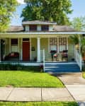 Charming bungalow with a front porch, rocking chairs, and lush greenery.