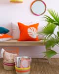 Yellow pendant light, orange leaf pillow on bench, round mirror, and colorful baskets on woven rug with green plant.