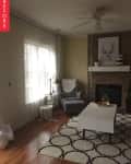Living room with gray armchair, white coffee table, patterned rug, and stone fireplace with deer artwork.