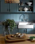 Farmhouse kitchen with blue cabinets, white sink, wooden countertop, and decor including hydrangeas and stacked dishes.