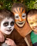 Three children with face paint resembling a panda, tiger, and giraffe, smiling outdoors.